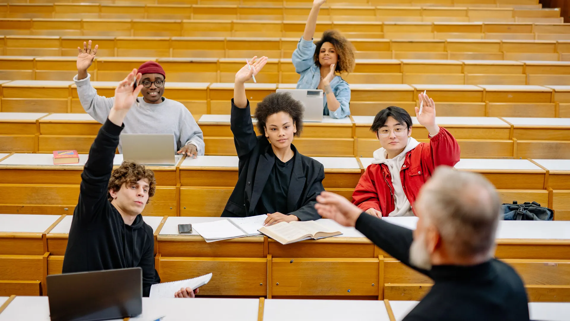 Students raising their hands during a lecture in a tiered teaching hall