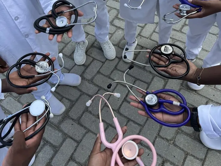Students in white coats standing in a circle, each holding a stethoscope